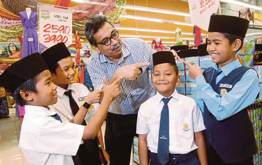 DR Abu Bakar (tengah) memakaikan songkok pada murid SK Krubong  di Mydin Mall, MITC Ayer Keroh, semalam.