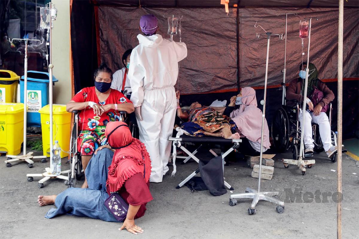 PETUGAS kesihatan  lengkap berpakaian PPE merawat pesakit di kawasan kecemasan di tempat letak kenderaan yang disediakan untuk menampung pesakit Covid-19 di sebuah hospital di Bekasi, Jawa Barat, Indonesia.