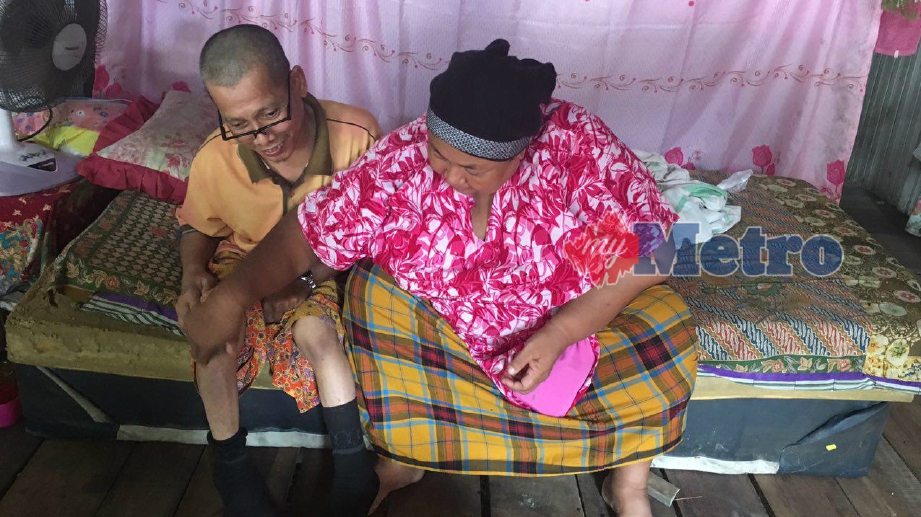 NIK Rozizah Daud, 49, menunjukkan kedua-dua kaki suaminya, Mat Zain Dollah, 56, yang lumpuh ketika ditemui di rumahnya di Kampung Belukar Limbat, Pasir Tumboh. FOTO Siti Nor Hidayatidayu Razali