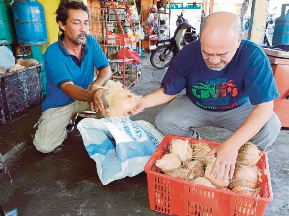 Shamsul Bokhari (kiri) menerima kelapa yang dijual Zakir di kedai runcitnya di Kampung Solok Duku, Masjid Tanah. 