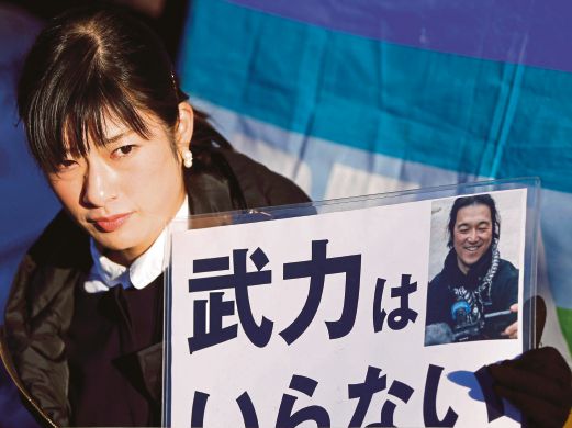 SEORANG wanita memegang gambar wartawan Kenji Goto ketika perarakan mengecam  Abe di depan kediaman rasminya di Tokyo, semalam.