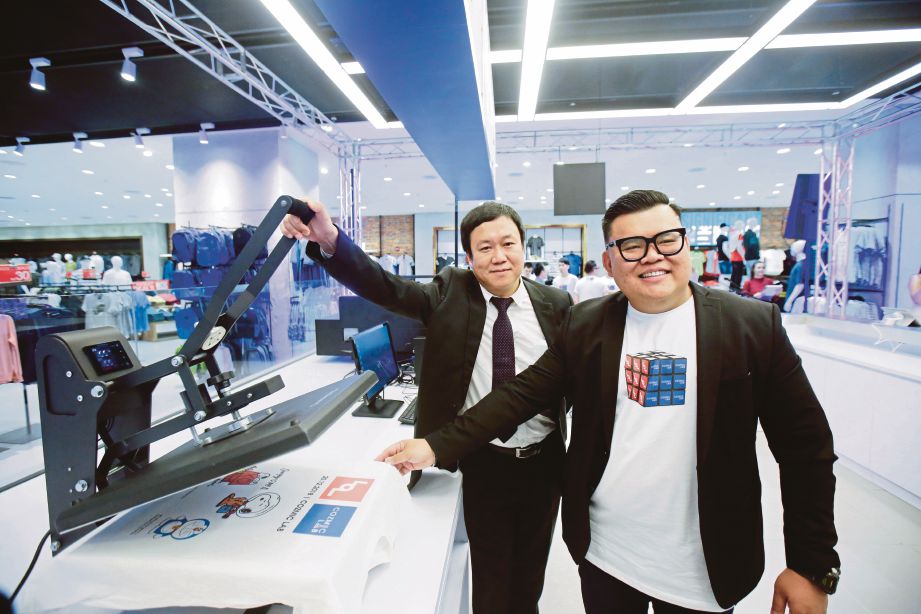 CHONG (kanan) bersama Segawa menunjukkan mesin pencetak pakaian pada majlis Pelancaran Cozmic Lab di Butik LOL di Putrajaya.