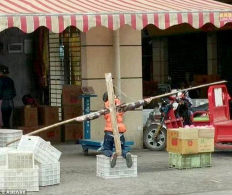 GAMBAR menunjukkan seorang budak lelaki berlutut dengan kedua-dua tangannya diikat pada kayu berbentuk salib di luar sebuah kedai di Chongqing, China. - Agensi