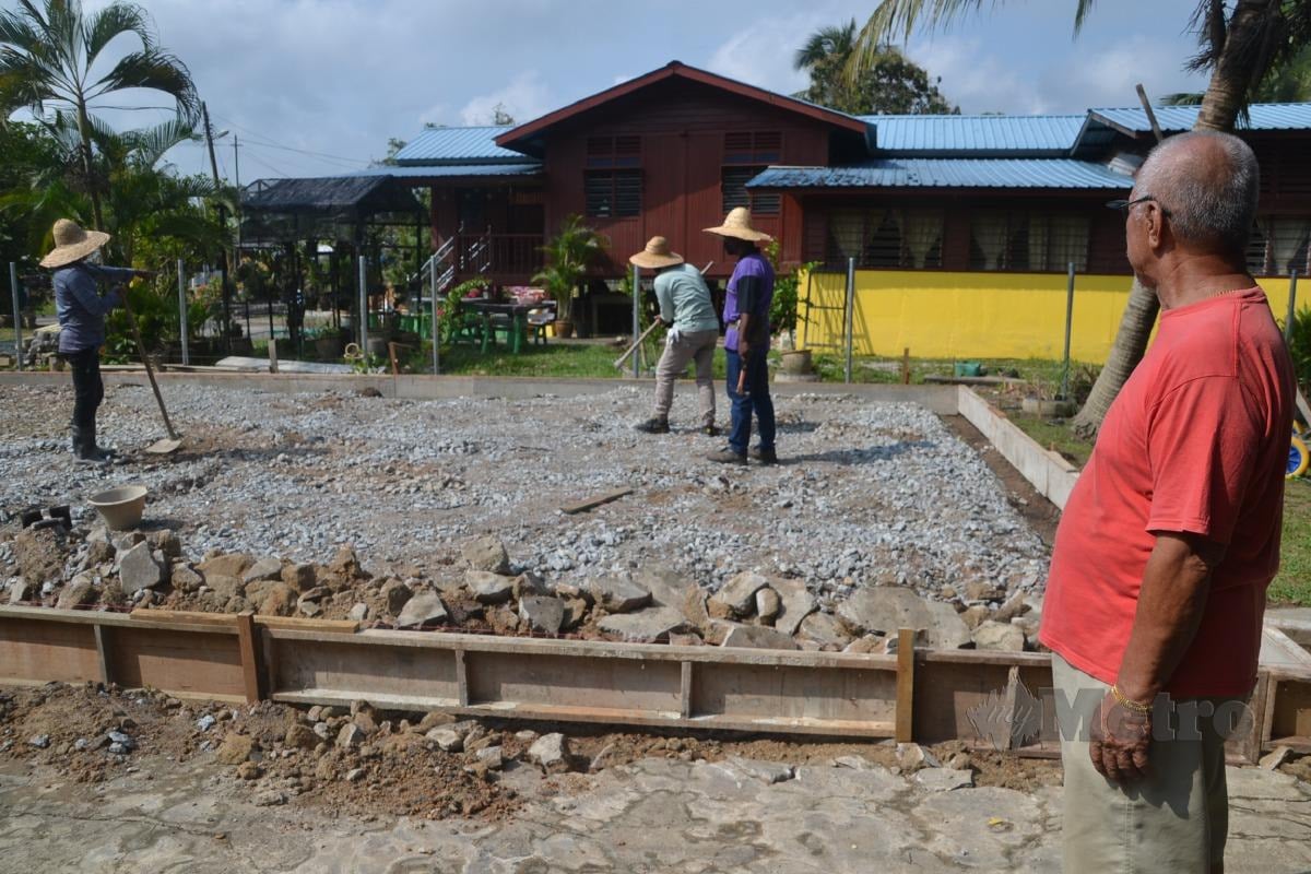 Yusof memerhatikan pekerja membina rumahnya bersebelahan rumah papannya yang rosak teruk akibat banjir di Kampung Telok Berembang, Lubok Cina dekat Masjid Tanah. FOTO Hassan Omar