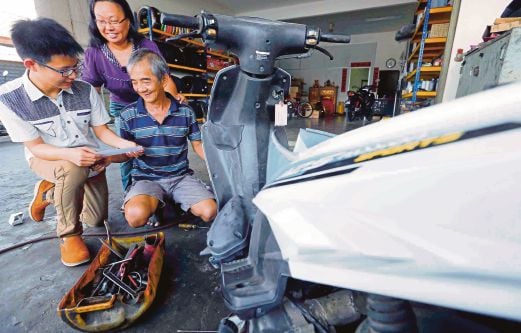 Neo (kiri) menunjukkan slip keputusan SPM kepada ayah dan ibunya di bengkel membaiki motosikal keluarganya di Batu 1, Jalan Langgar.