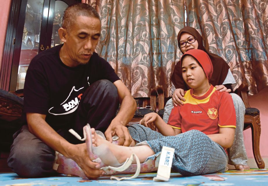  Razali bersama isteri, Siti Aishah  membantu Nuraina Syafiqah memakai alat terapi di kaki. 