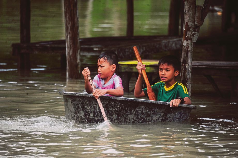   GAMBAR dirakam 1 Januari lalu menunjukkan dua kanak-kanak mendayung meredah banjir selepas hujan lebat di Narathiwat.  - AFP
