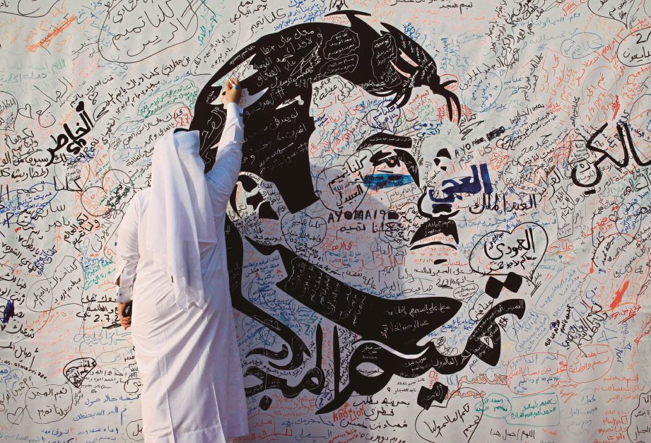 SEORANG lelaki menulis pada lukisan yang menggambarkan Emir Qatar,  Sheikh Tamim Bin Hamad Al-Thani di Doha, semalam.  - Reuters 