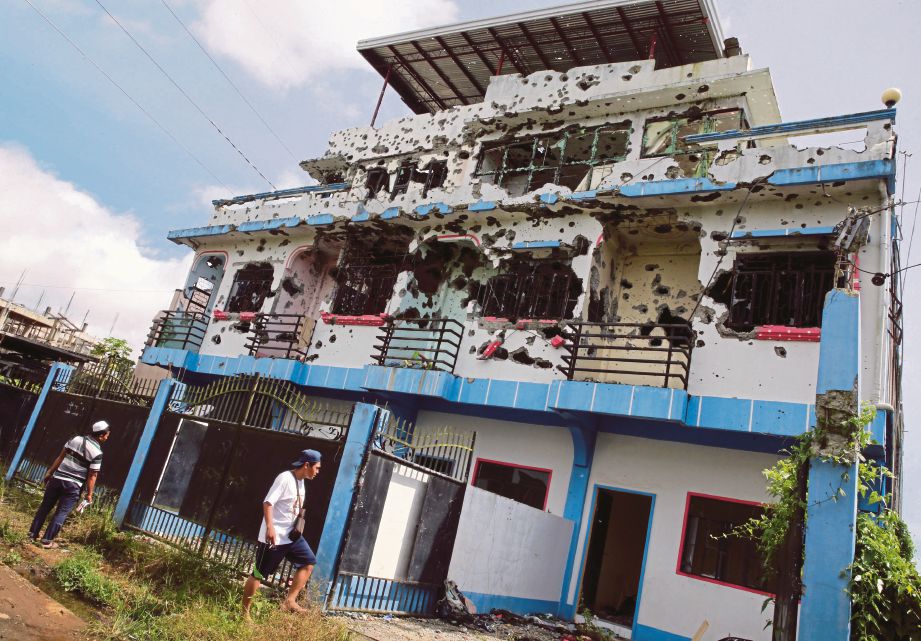 PENDUDUK melihat sebuah bangunan kediaman yang penuh dengan kesan tembakan akibat pertempuran di daerah Malutlut di Marawi. - Reuters