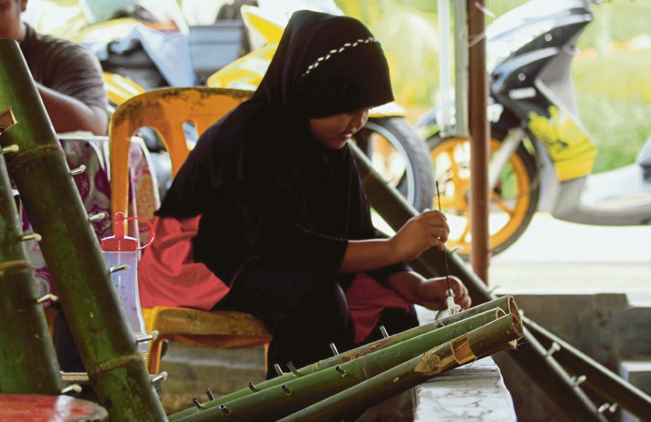 NUR Sumayyah Abdullah, 10, turut membantu  memasukkan sumbu pelita buluh di Kampung Belimbing Dalam, Durian Tunggal. 