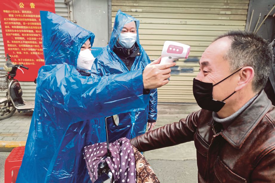 SEORANG pekerja memeriksa suhu badan  lelaki di pintu masuk kawasan perumahan. FOTO Reuters
