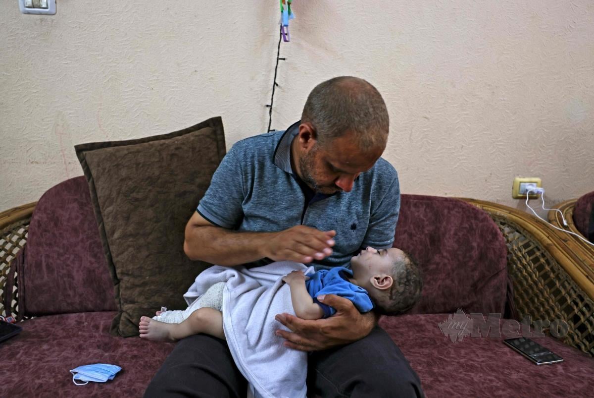 WARGA Palestin, Mohammad al-Hadidi memangku anaknya yang terselamat selepas diserang tentera Yahudi. Manakala isteri dan empat lagi anaknya syahid dalam serangan itu. FOTO AFP