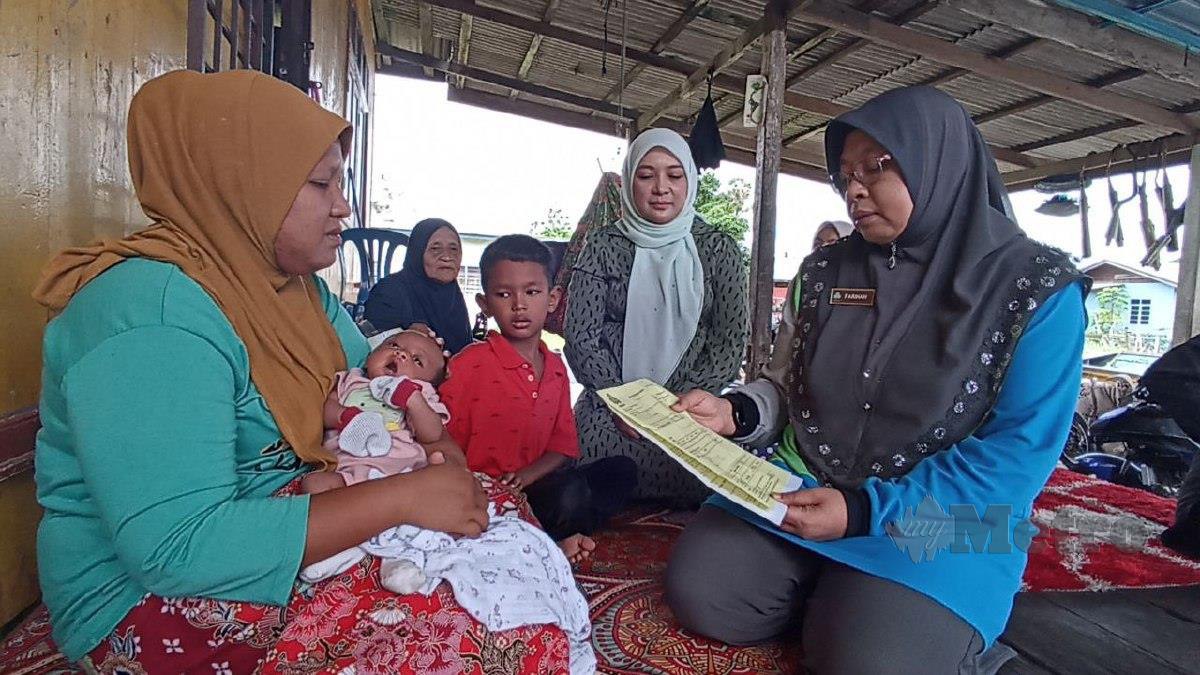 Farihah (kanan) dan Nor Hasma Yanty (tengah) ketika menyantuni keluarga Nurul Akmmar bagi menyampaikan Faedah Pencen Penakat dan Faedah Pengurusan Mayat di rumah mentuanya di Kampung Tanjung, Batu Rakit. FOTO ZAID SALIM