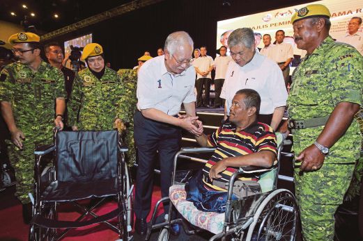 NAJIB bersalaman dengan penerima kerusi roda, Sutomo Moran sambil disaksikan Dr Ahmad Zahid, semalam.