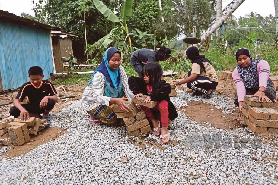 SURIATI (tengah) bersama empat anak dan adiknya menyusun batu-bata tapak rumah selepas kediamannya dihanyutkan arus banjir di Kampung La. FOTO Ghazali Kori