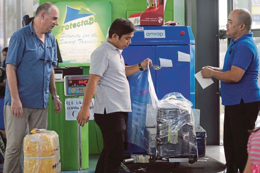DUA penumpang membalut bagasi dengan plastik di lapangan terbang Manila semalam bagi mengelak objek asing dimasukkan ke dalam beg mereka.