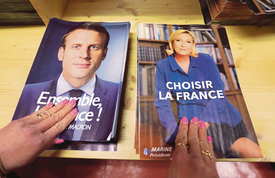PETUGAS menyiapkan dokumen untuk pengundi menjelang pilihan raya pusingan kedua Presiden Perancis Ahad ini.  Dokumen itu mengandungi manifesto kedua-dua calon, Macron (kiri) dan Le Pen.  - Reuters 