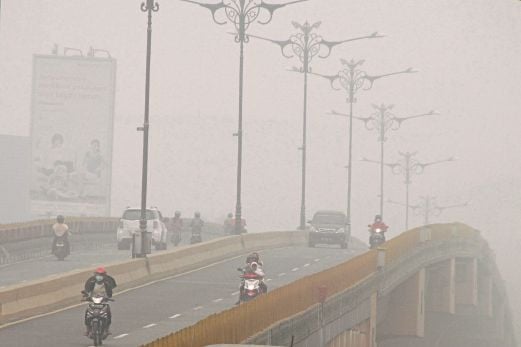 KERETA dan motosikal dilihat melintasi sebuah jambatan di Pekanbaru, Riau, kelmarin, dengan keadaan jerebu tebal.  