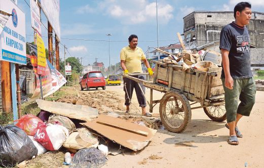 AZAM (kiri)  bersama anaknya mengangkut sampah selepas membersihkan rumah mereka daripada sisa banjir di Kampung Cina.