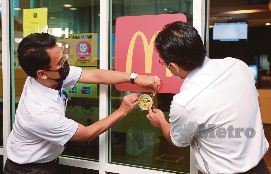 SAIPOLYAZAN (kiri) dan Azhar menampal stiker zakat pada dinding restoran McDonald di Mutiara Damansara, semalam.