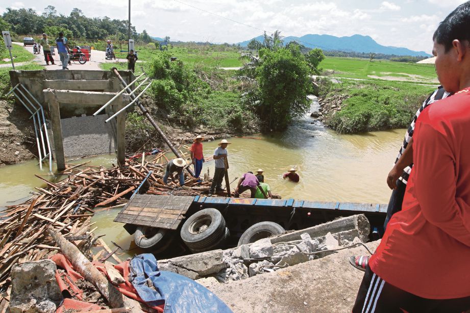 KERJA memunggah lori muatan kayu yang terhumban ke dalam tali air selepas jambatan itu runtuh akibat hakisan banjir.