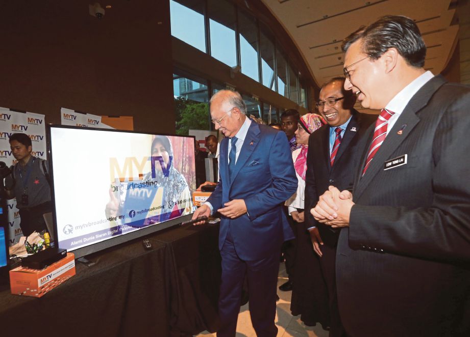 NAJIB   mencuba alat kawalan jauh televisyen MYTV sambil diperhatikan Dr Mohd Salleh   (dua dari  kanan) dan Menteri Pengangkutan  Datuk Seri Liow Tiong Lai (kanan) pada pelancaran myFreeview.