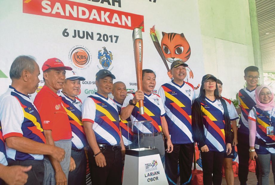 JAMES (tengah) meletakkan obor KL2017 selepas berlari dari Masjid Daerah Sandakan hingga ke Padang Bandaran Sandakan.