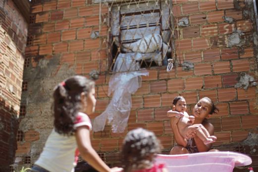 Rosana Vieira Alves (kanan) memandikan anaknya, LuanaVieira yang menghidap mikrosefali, sementara dua anaknya yang lain bermain di luar rumah mereka di Olinda, Brazil.  Penyakit itu yang menyebabkan bayi dilahirkan dengan kepala kecil ada hubungan dengan Zika, virus bawaan nyamuk.