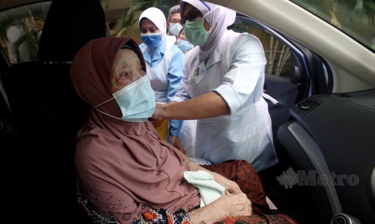 Warga emas Che Ah Taib yang  berusia 100 tahun menerima suntikan vaksin COVID-19 secara pandu lalu ketika hadir dibawa anak lelakinya, Salim Saad, 64, secara  'walk-in' di Pusat Pemberian Vaksin (PPV) Dewan Millenium di Kepala Batas. FOTO DANIAL SAAD