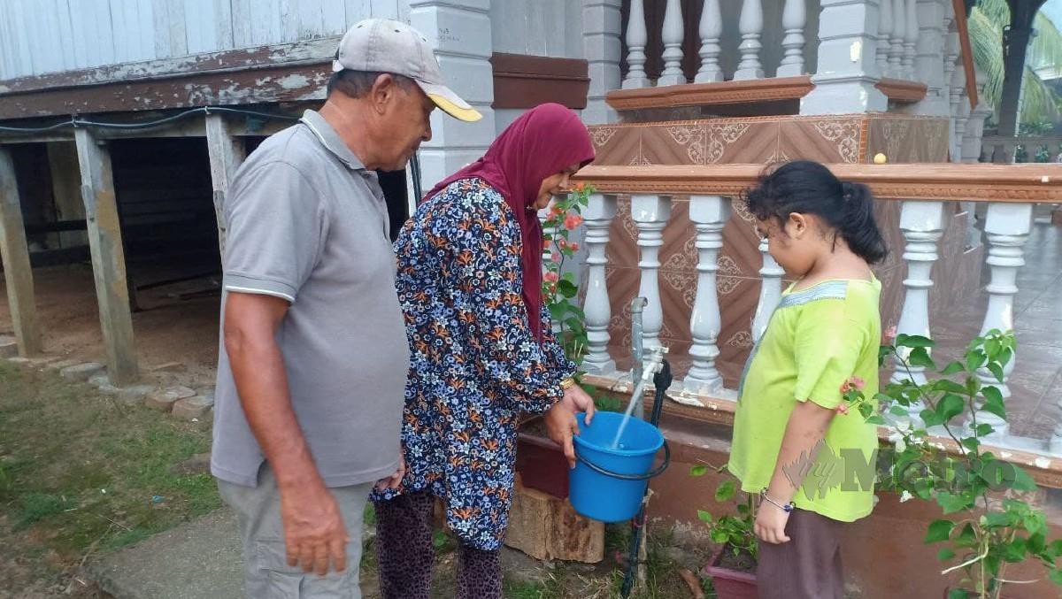  Suri rumah, Napisah Abdul Wahab bersama suami, Ramli Ismail dan cucunya dari Kampung Jeram, Manir gembira selepas bekalan air bersih kembali pulih sesudah 12 hari terganggu. FOTO Malik Muhamad