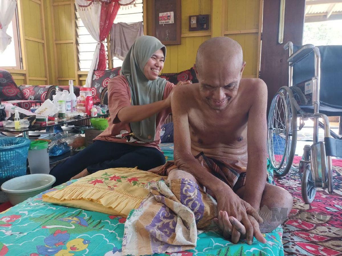 Suriani Kamarudin, 33, mengelap badan suaminya, Razi Ahmad, 49, yang menghidap kencing manis, buah pinggang tahap empat dan diserang strok ketika ditemui di rumah mereka di Kampung Kedai Buloh di sini. FOTO SITI ROHANA IDRIS