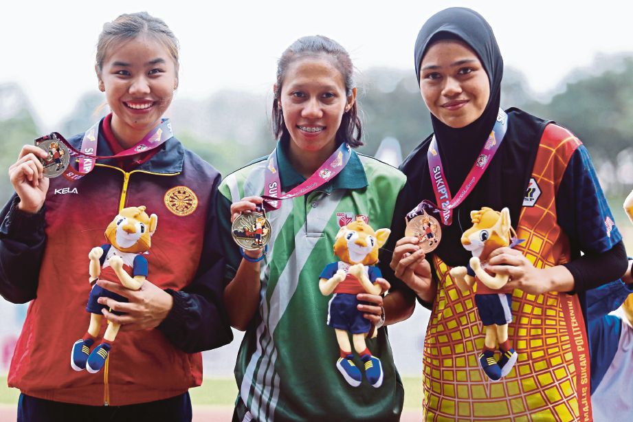 HUSNIAH (tengah) memperagakan pingat emas acara 100m dimenanginya.