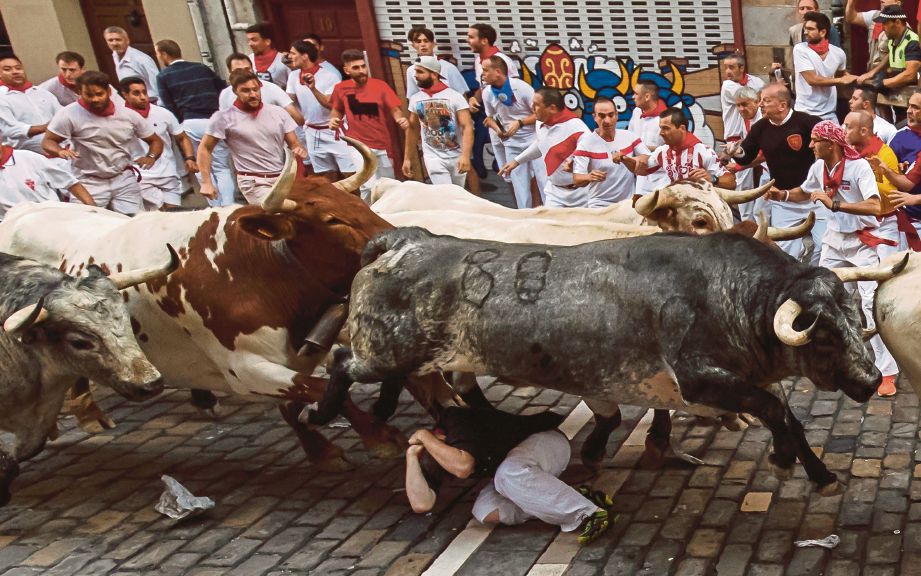 SEORANG peserta terjatuh dirempuh lembu pada hari pertama festival larian lembu San Fermin. - AFP 