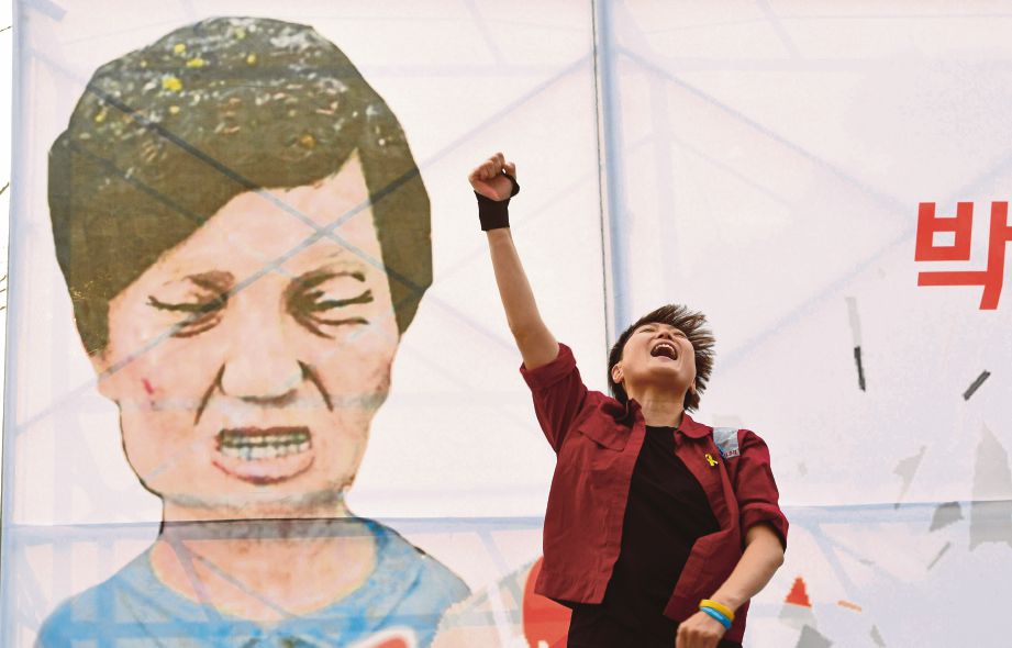 SEORANG penunjuk perasaan melaungkan slogan di depan lukisan karikatur Park  ketika perhimpunan menggesa pendakwaan presiden itu di Seoul, semalam. - AFP 