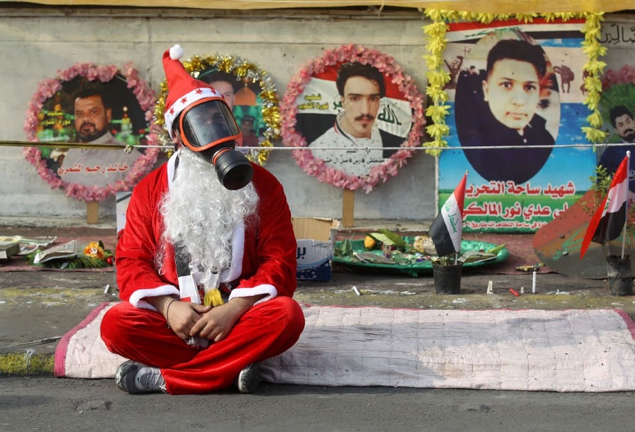 SEORANG penunjuk perasaan berpakaian seperti Santa Claus dengan topeng gas duduk memprotes di depan gambar rakannya yang terbunuh dalam protes antikerajaan. FOTO AFP
