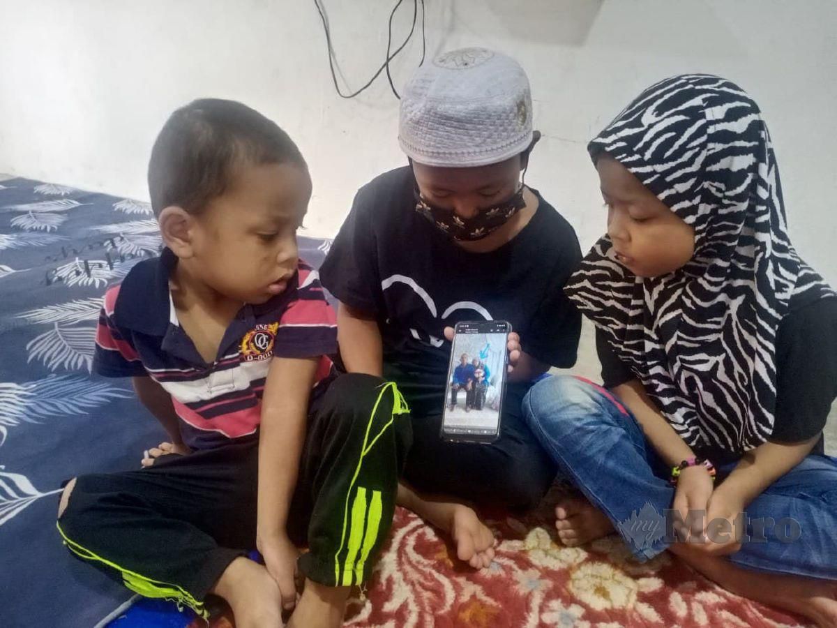 Muhammad Amar Mohd Zamani,11, menunjukkan gambar ibu bapanya kepada dua orang adiknya Nur Alia,8, dan Muhammad Amsyar,4, di rumah mereka di Kampung Belantik di sini. FOTO Noorazura Abdul Rahman
