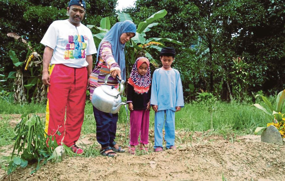 MASKAH ditemani dua anaknya menyiram air mawar di atas pusara arwah suaminya Zarani di Tanah Perkuburan Islam Kampung Prak, Gua Musang, kelmarin.