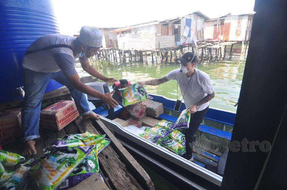 BENEDICT (kanan) bersama  penduduk Kampung Pondo memunggah barangan keperluan yang dibawa menaiki bot sebelum diberikan kepada penduduk kampung. FOTO Yun Mikail