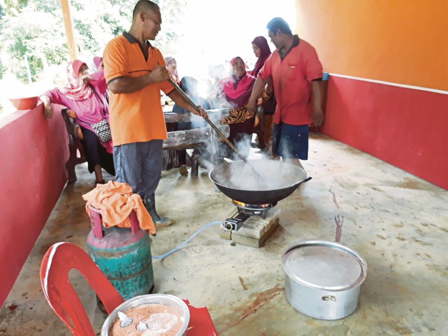 ROSMIZAN (kanan) melihat penduduk kampung bergotong-royong memasak makanan kenduri doa selamat selepas dilanda banjir kilat.