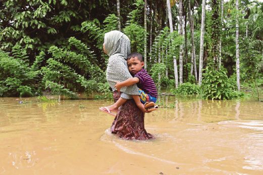 SEORANG ibu membawa anaknya meredah banjir di Agam. 