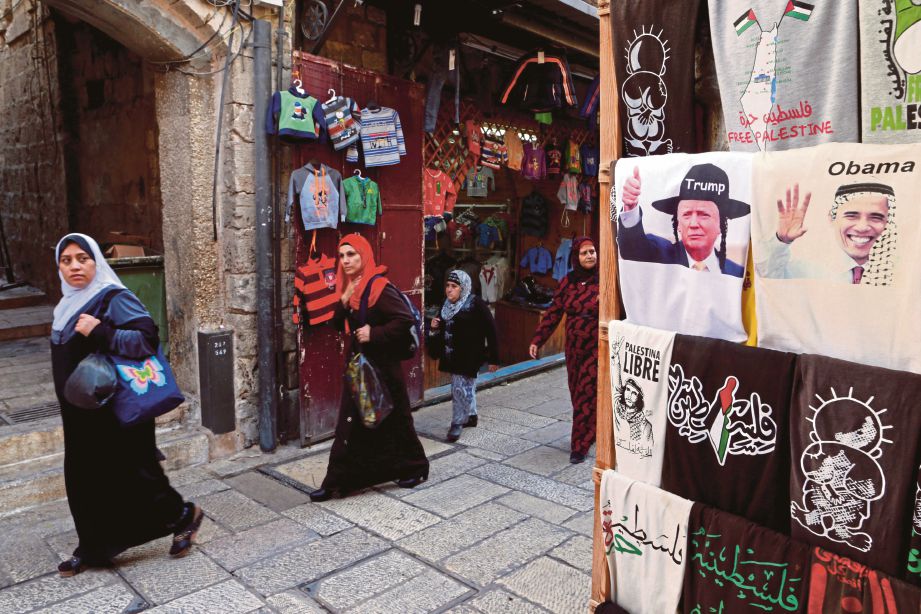 WANITA Palestin berjalan melintasi kedai menjual kemeja-T dengan gambar Trump memakai topi Yahudi di sebelah baju dengan imej Presiden Barack Obama di Baitulmaqdis, semalam.  - Reuters