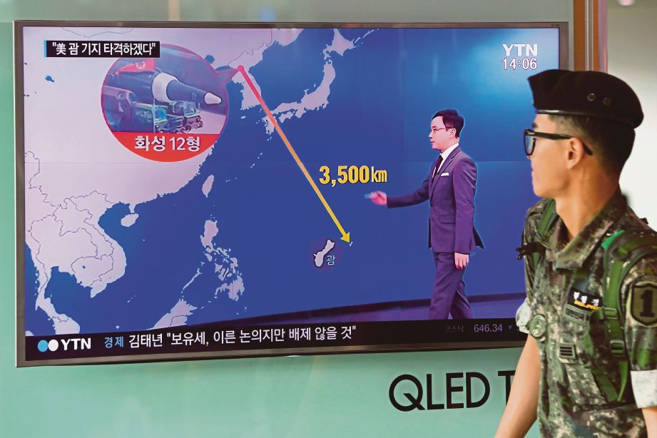 SEORANG askar Korea Selatan berjalan melintasi skrin televisyen yang menunjukkan grafik jarak antara Korea Utara dan Guam di sebuah stesen kereta api di Seoul, semalam.  - AFP 