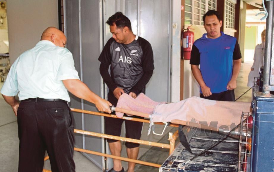 EH Pian (tengah) mengangkat mayat abangnya di bilik forensik Hospital Kelaburan, Tumpat, semalam.