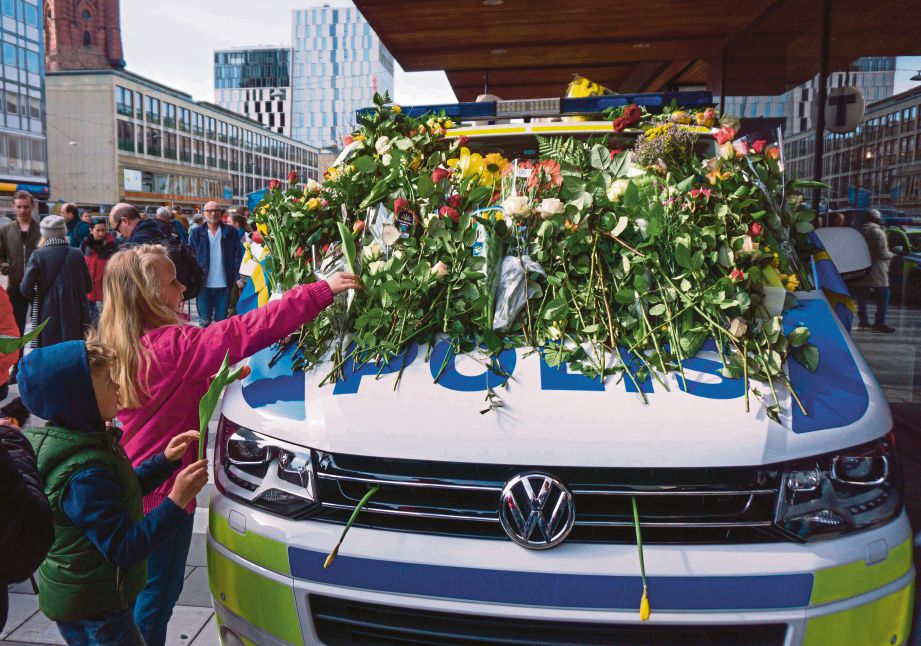 KANAK-KANAK meletakkan bunga di atas kereta polis di tempat sebuah trak merempuh pejalan kaki di sebuah pasar raya di Stockholm, Sweden, Jumaat lalu. - AFP 