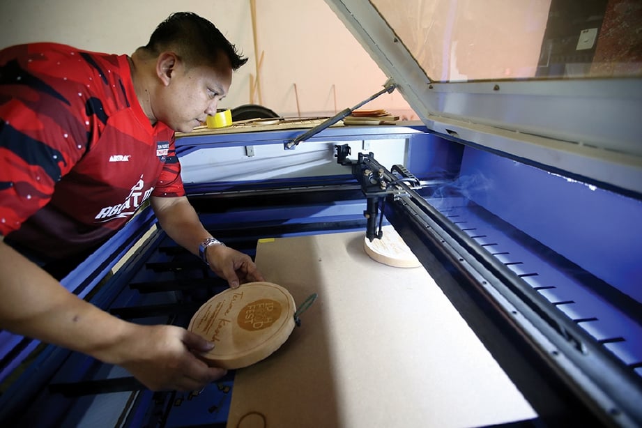 YU Azman memeriksa proses mengukir kraf kayu yang dihasilkan mesin laser.