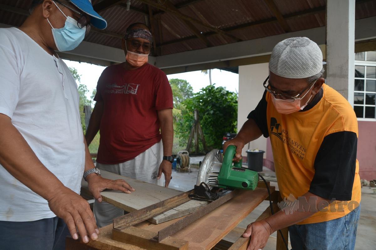 Julasapiyah memotong papan untuk membuat keranda sambil dibantu ahli  Persatuan Permuafakatan Penduduk Islam Kuala Sungai Baru, Masjid Tanah. FOTO Hassan Omar