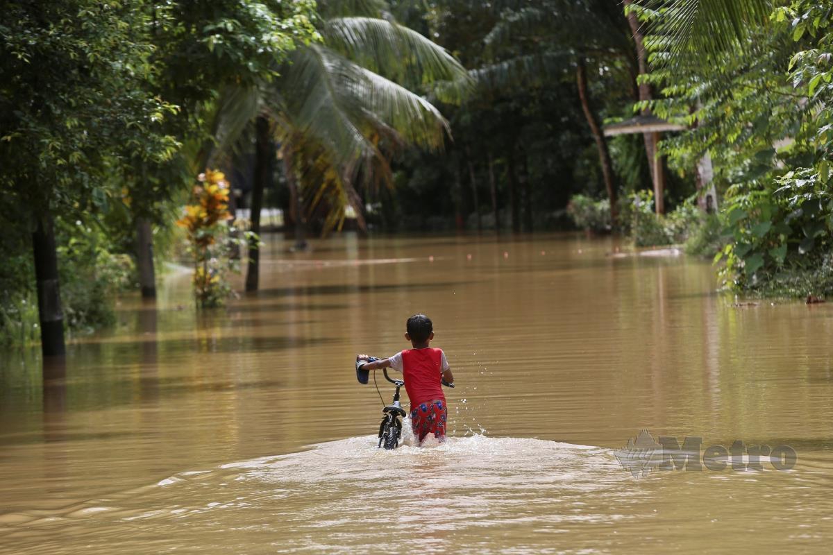 SEORANG kanak-kanak menolak basikal meredah banjir ekoran hujan lebat sejak semalam di Kampung Pelong. FOTO GHAZALI KORI