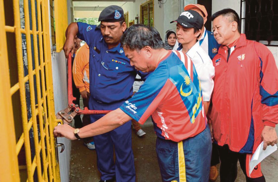 Yeo (dua dari kiri) dan pegawai DBKK memecahkan pintu rumah tidak berpenghuni selepas mendapat perintah mahkamah buat pemeriksaan kebersihan di Taman Public Jaya, Likas. 
