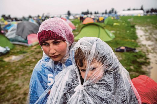 SEORANG pelarian wanita mendukung anak lelakinya yang dibungkus dalam plastik untuk mengelak basah dalam hujan di Idomeni.
