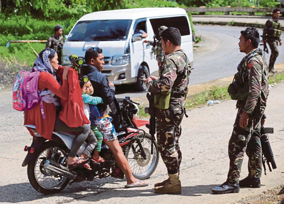 PASUKAN keselamatan Filipina memeriksa seorang lelaki dan keluarganya di satu sekatan jalan raya di bandar Marawi semalam ketika tentera kerajaan meneruskan serangan untuk menawan bandar itu daripada militan Maute, semalam. - Reuters 